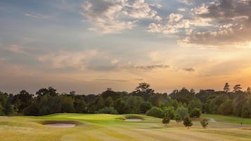 A golf course with sand bunkers, trees, and a clear sky.