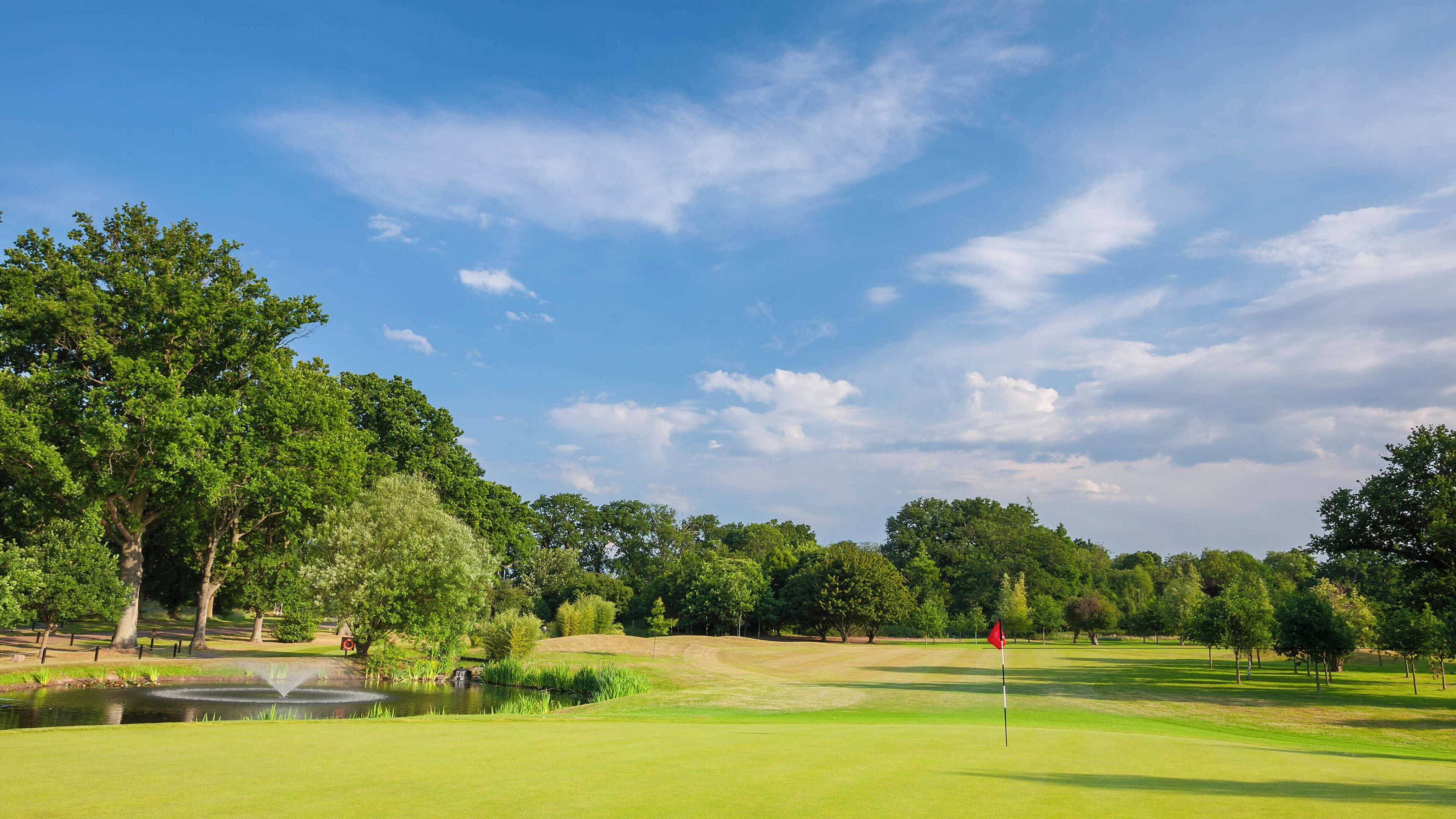 Un parcours de golf avec un étang, des arbres et un ciel dégagé.