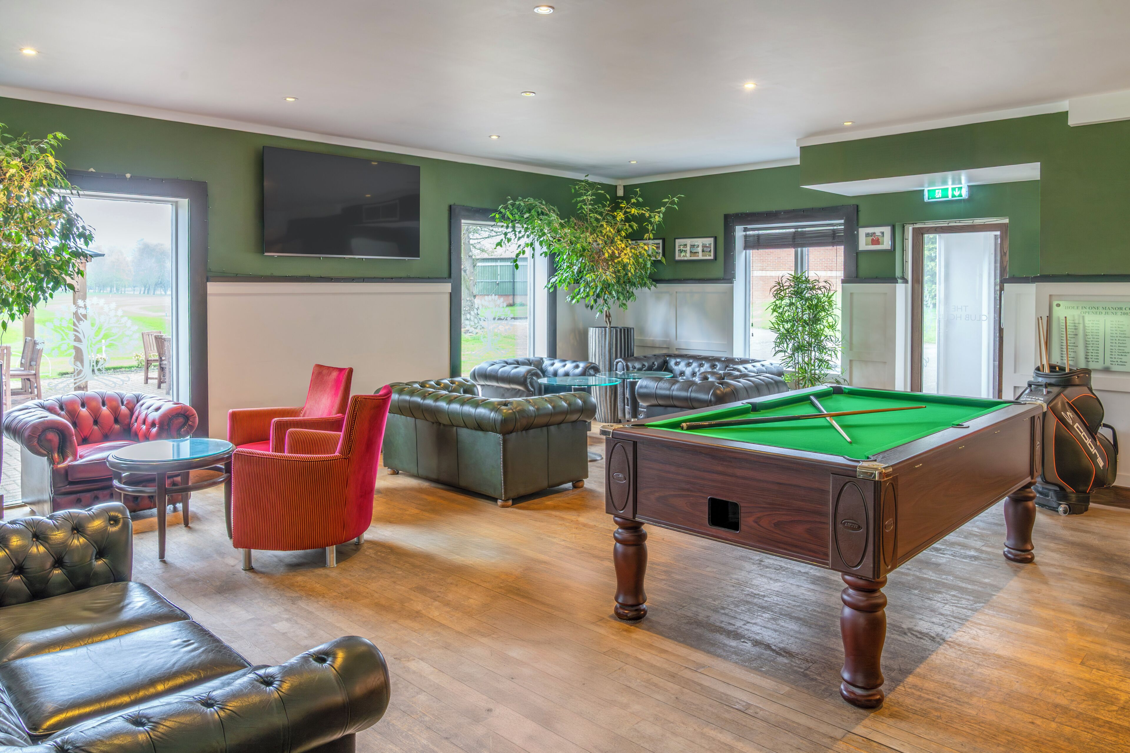 A pool table in a room with green walls, leather sofas, and a large window.