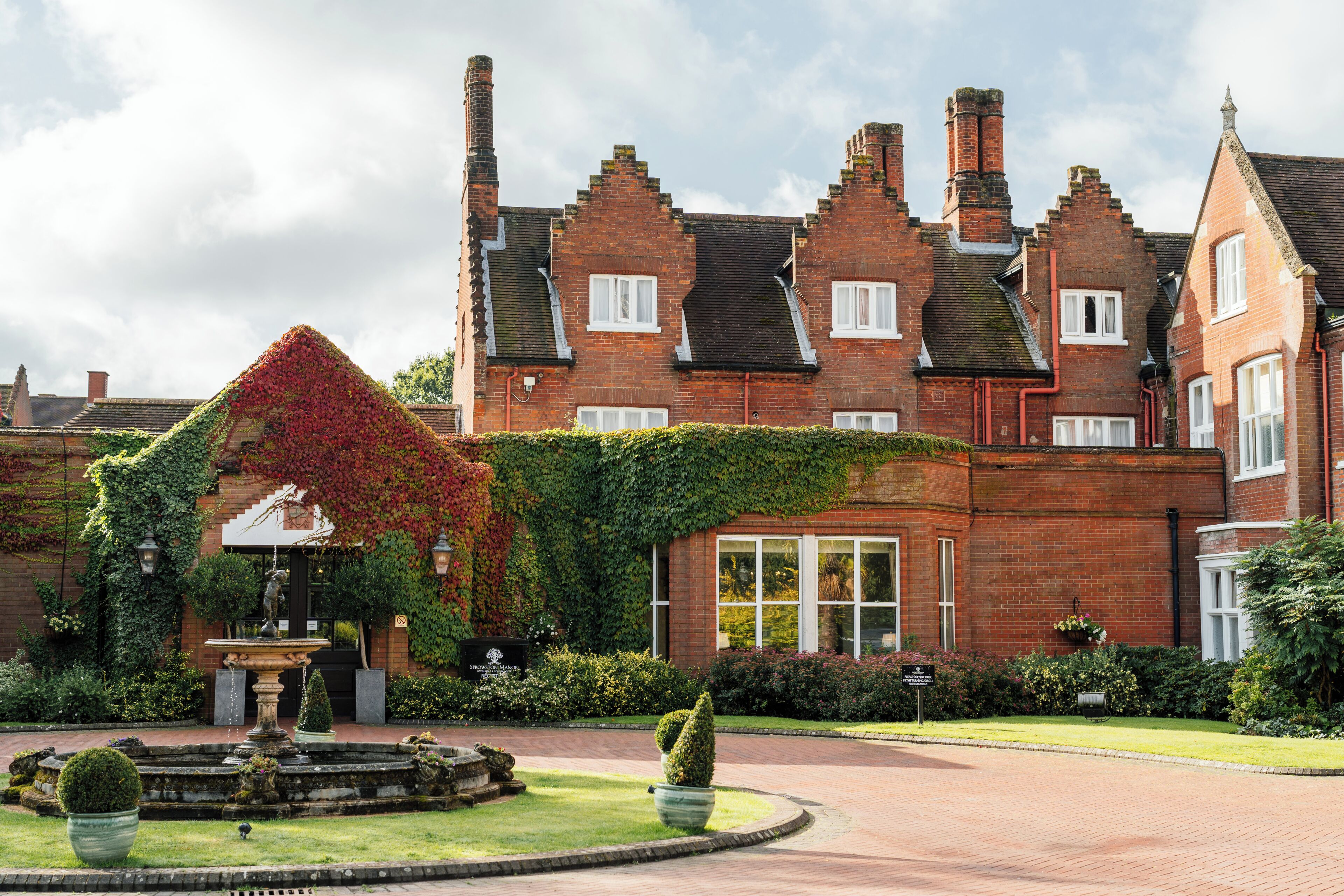 A large brick building with a garden, a fountain, and a well-maintained lawn.