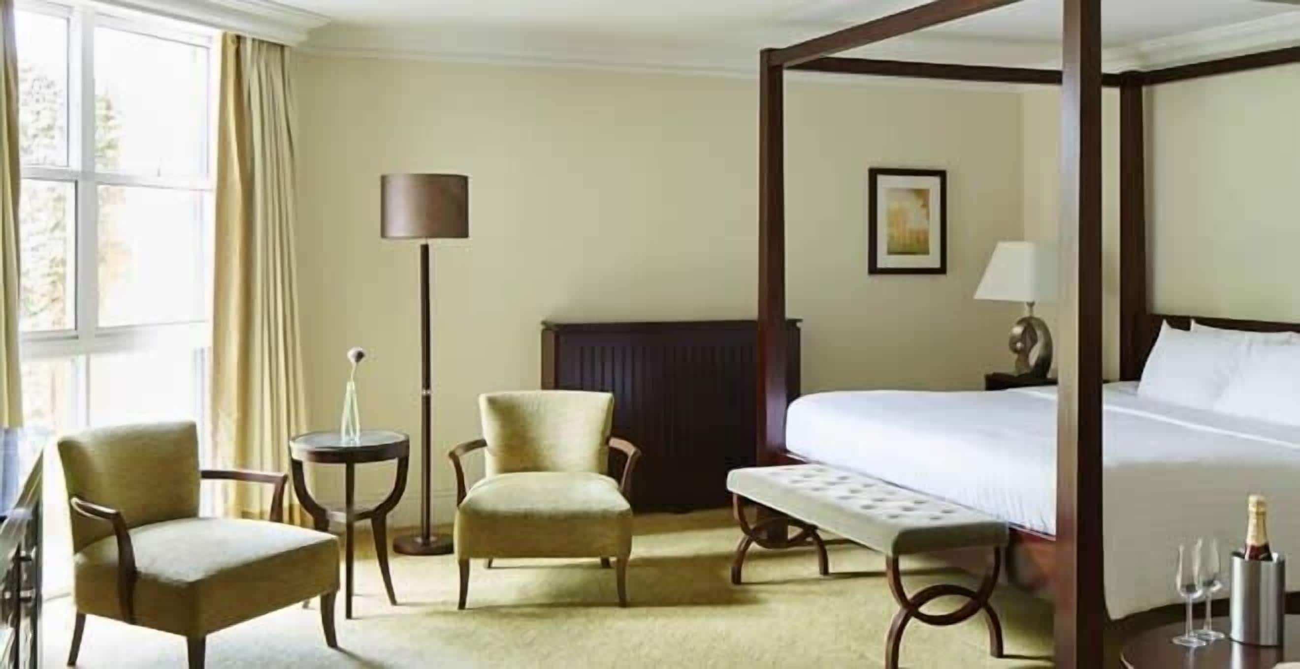 Una cama con dosel, dos sillones, una mesita y una lámpara de noche en una habitación de hotel.