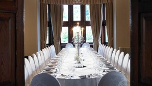 A long dining table set for a formal meal, with a chandelier and curtains in a room with wooden beams and large windows. - Sprowston Manor Hotel, Spa & Golf (Norwich)