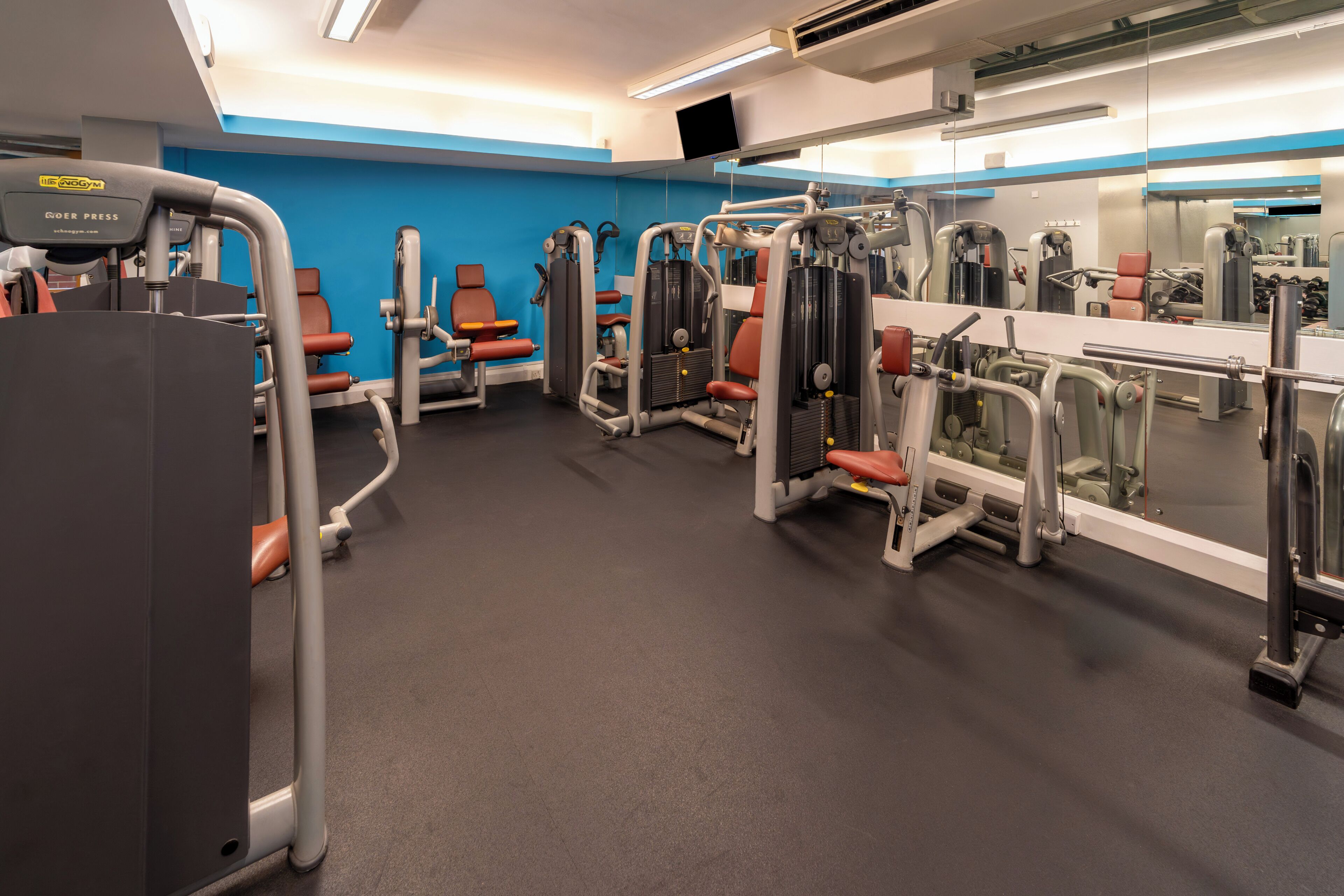Un gimnasio con máquinas de ejercicio, un espejo y paredes azules.