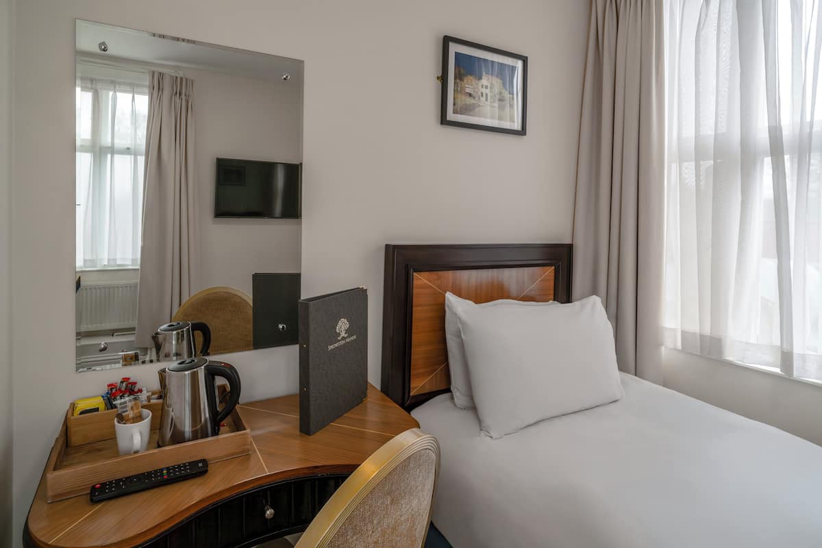 A hotel room with a bed, a desk with a coffee maker, a remote control, and a framed picture on the wall.