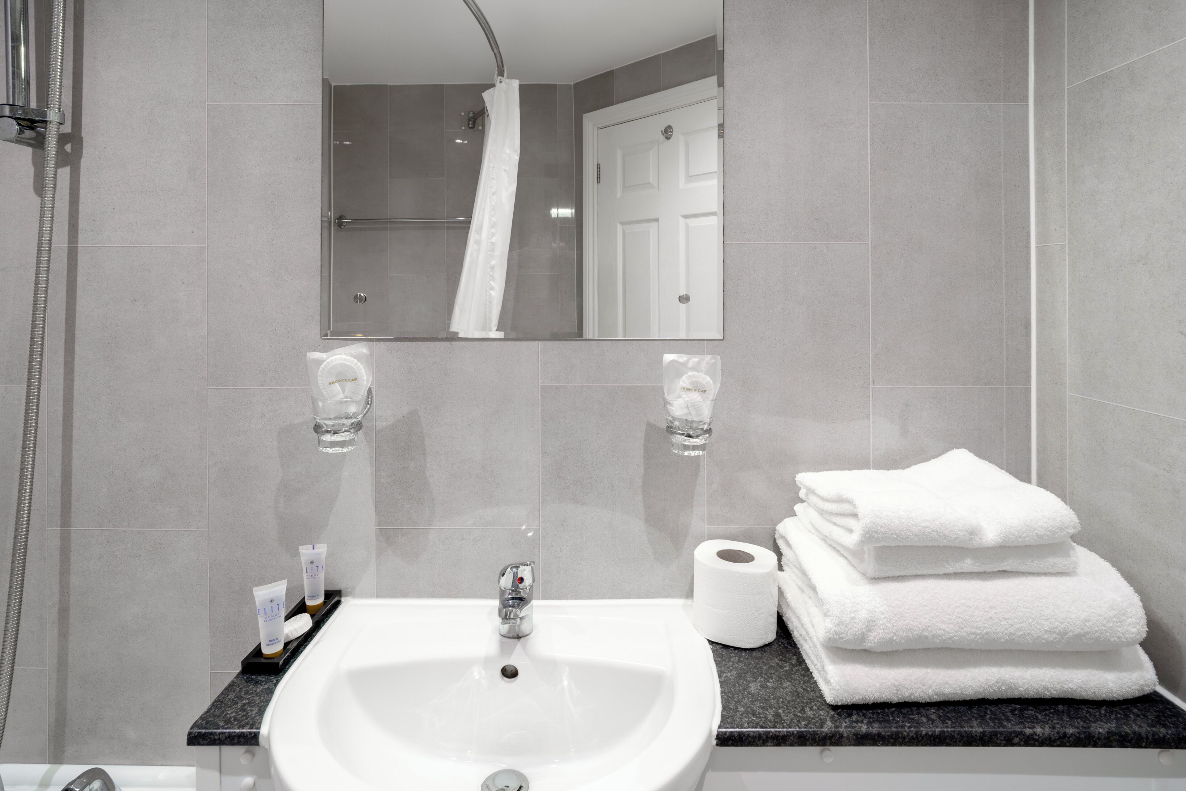 A bathroom with a sink, mirror, shower, and towels.