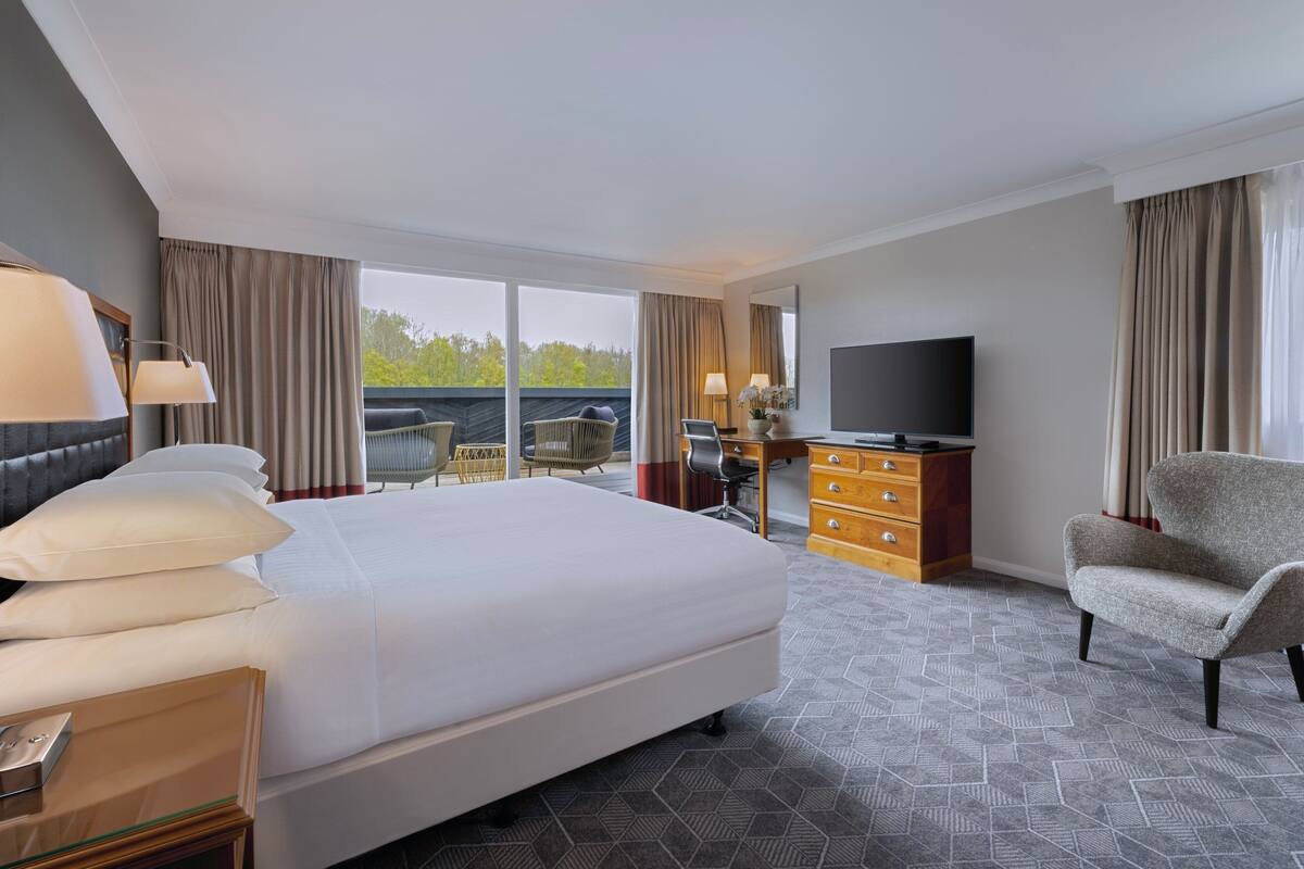 A hotel room with a large bed, a desk with a chair, a TV, and a view of the outdoors.
