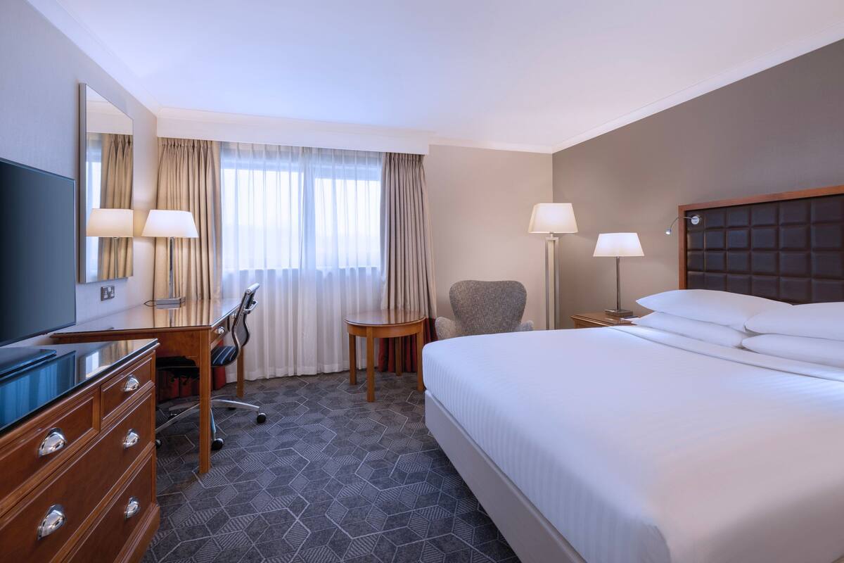 A hotel room with a large bed, a desk with a chair, a television, and two lamps.