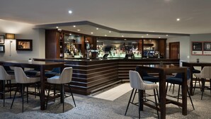 A bar area with a curved counter, bar stools, and a variety of bottles and glasses. - Delta Hotels by Marriott Northampton (Northampton)