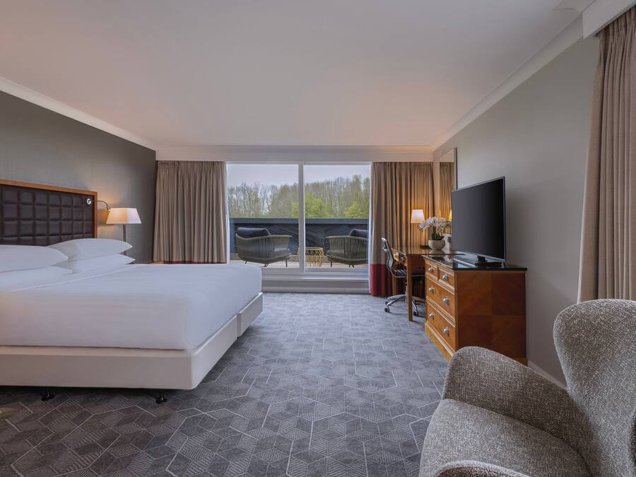 Una habitación de hotel con una cama grande, un escritorio con televisor y vistas al exterior a través de un ventanal corredero.