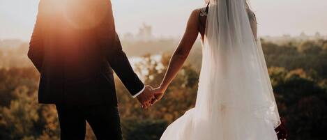 A couple holding hands in a field with a sunset in the background.