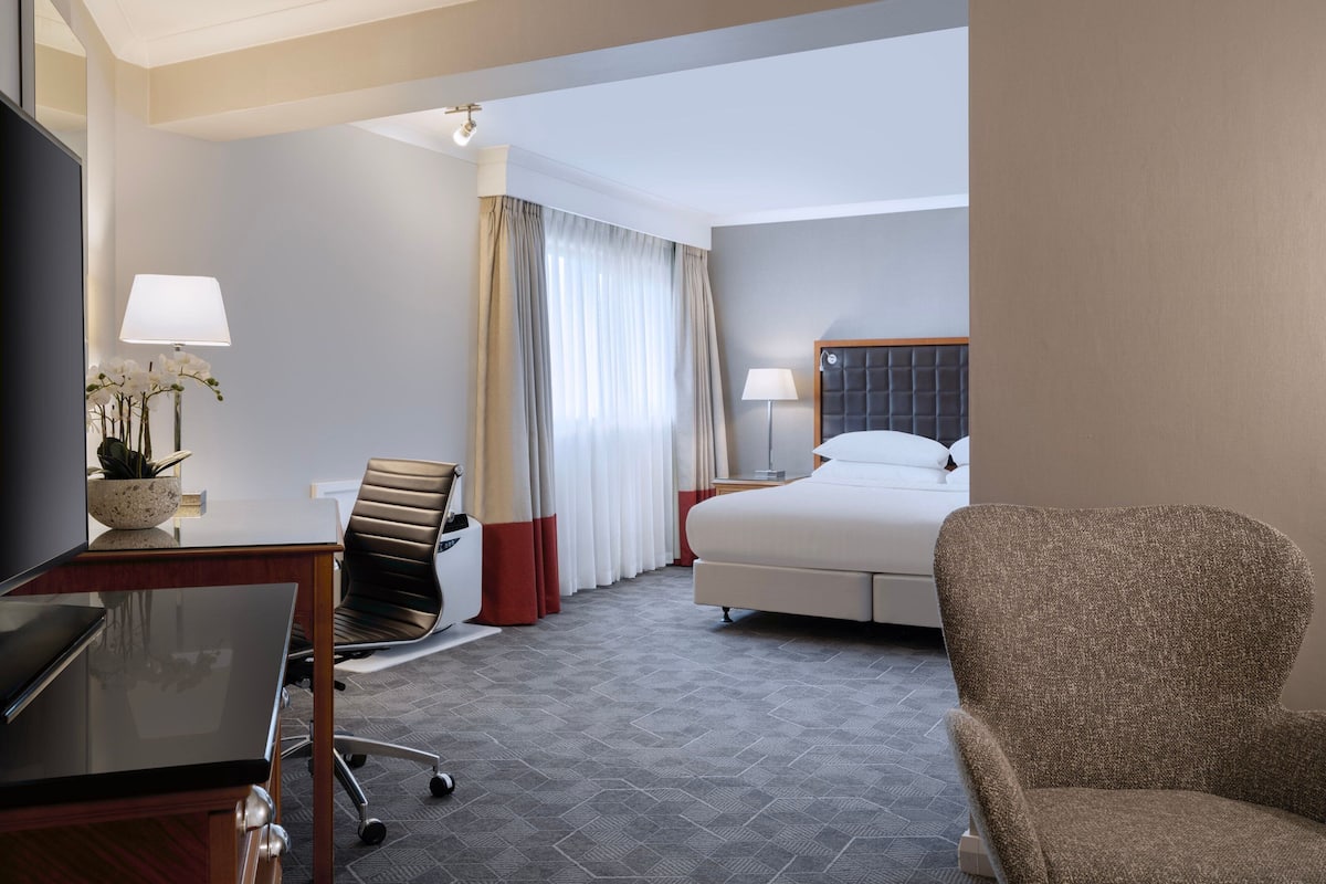 A hotel room with a bed, a desk, a chair, and a TV.