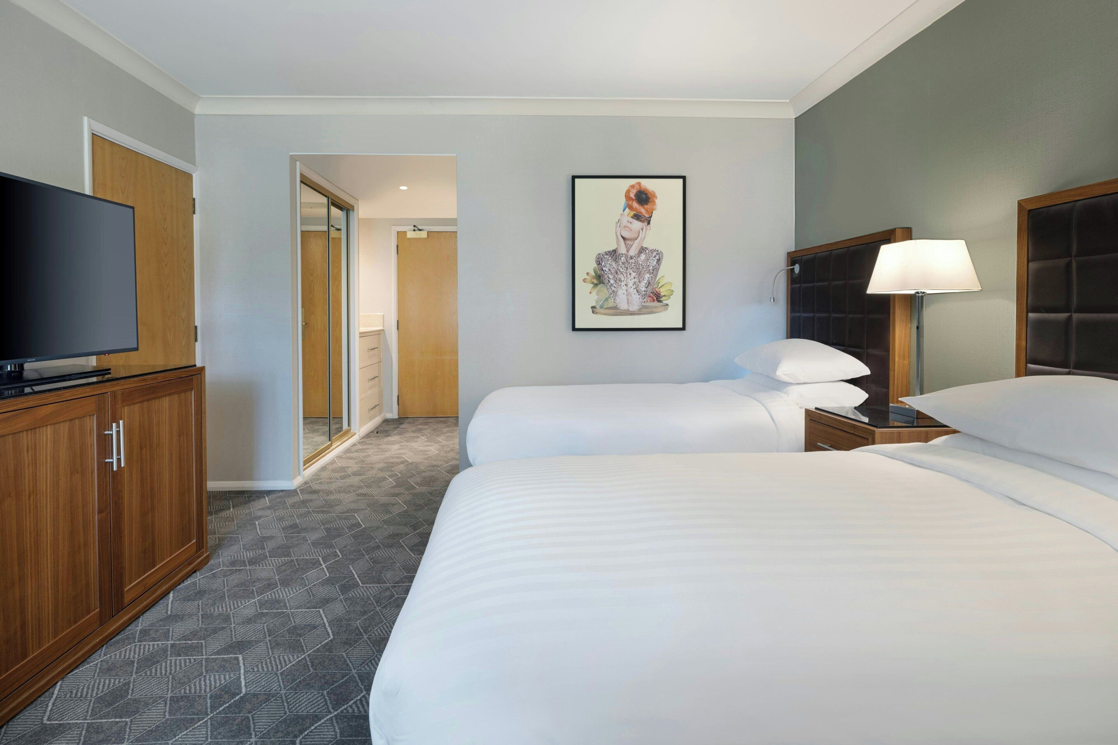 A hotel room with a large bed, a television, a framed artwork on the wall, and a bedside table with a lamp.