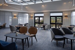 A modern hotel lobby with multiple seating areas, large windows, and a skylight.