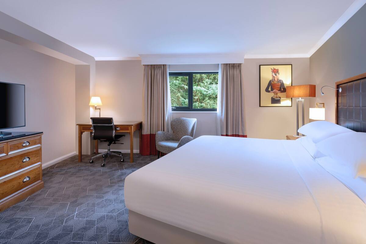 A hotel room with a large bed, a desk with a chair, a TV, and a window with curtains.