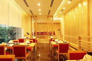 Un restaurante con una barra alargada, sillas rojas acolchadas y vistas a árboles a través de amplios ventanales.