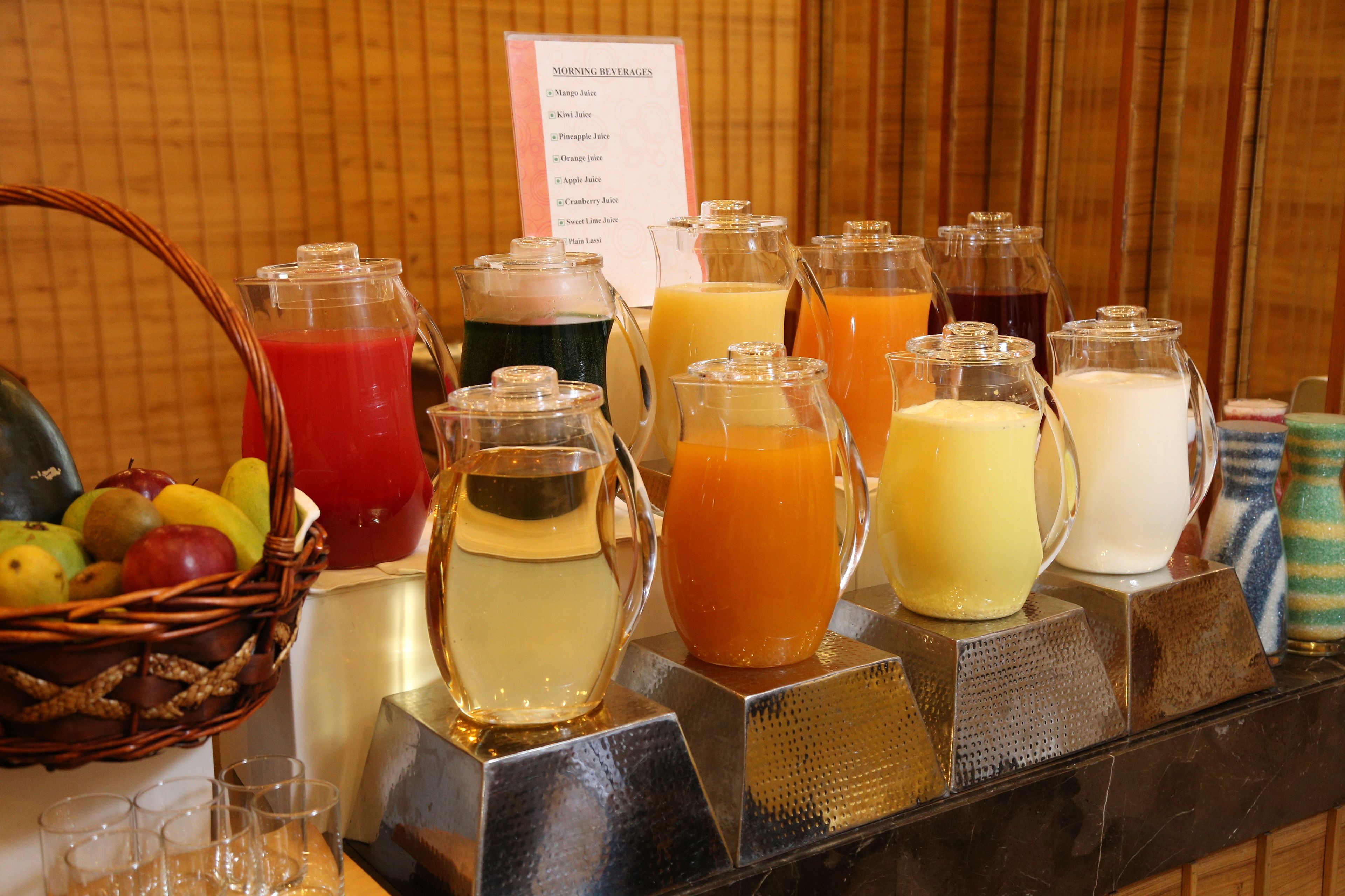 A breakfast buffet with various fruit options and a sign listing available juices.
