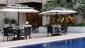 An outdoor dining area with tables and chairs, umbrellas, and a pool.