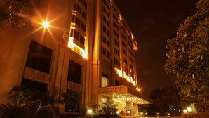 A multi-story hotel with a grand entrance, illuminated by warm lighting, surrounded by landscaped gardens and palm trees.