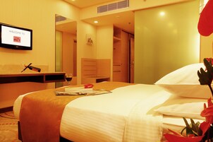 Habitación de hotel con una cama, un televisor mostrando “BIENVENIDOS AL MET” y una barra minibar, además de una puerta que da a un baño.