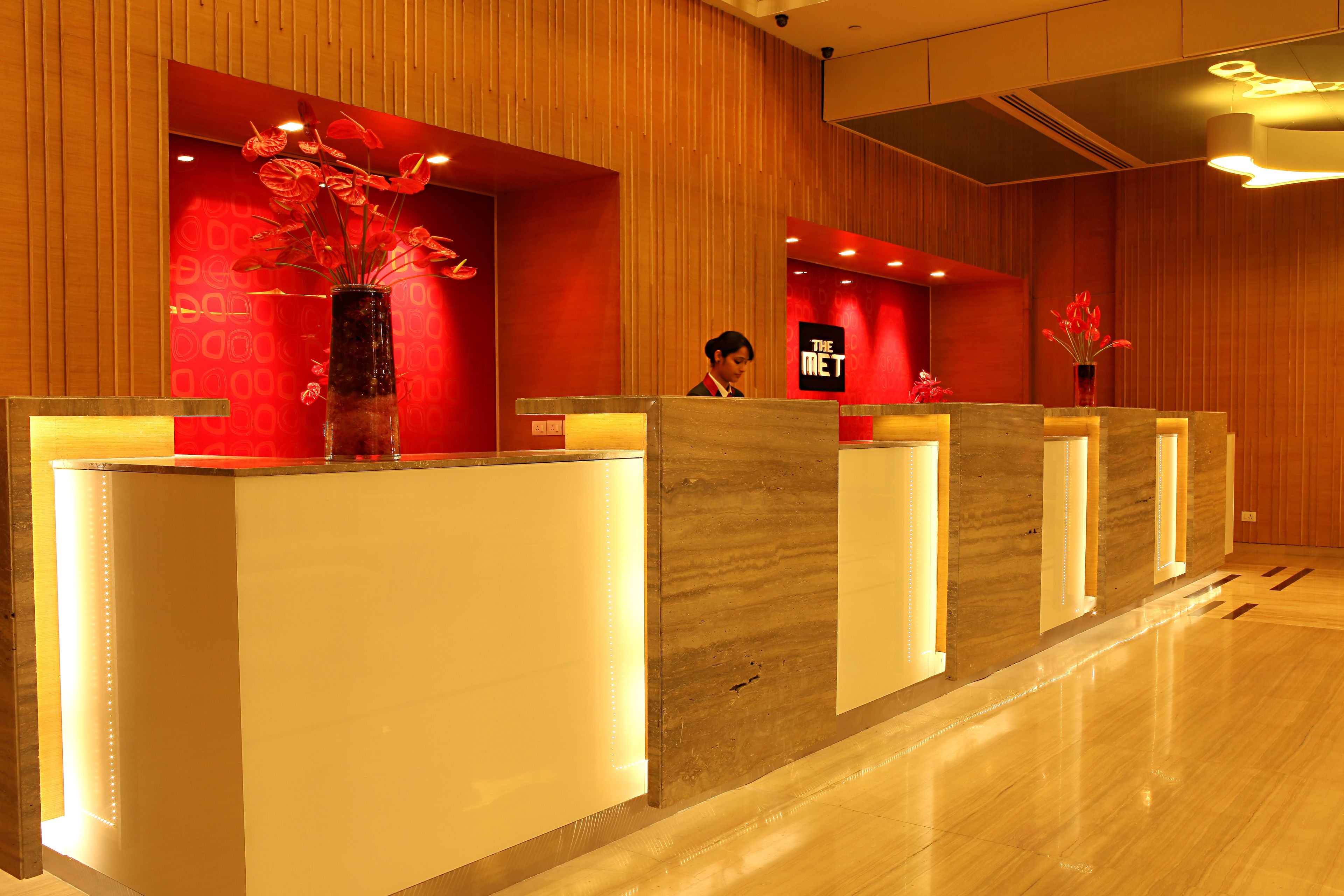 A hotel reception area with a wooden interior, multiple reception desks, and red floral decorations.