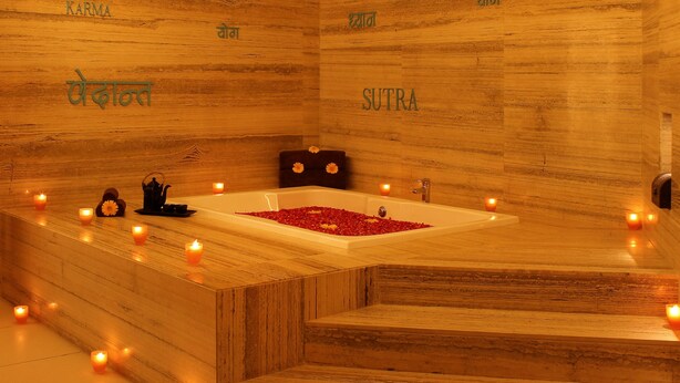 A wooden bath area with a bathtub filled with rose petals, candles, and a black teapot.