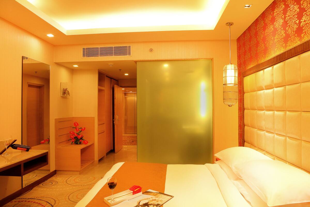 Une chambre d’hôtel avec un lit, une table de chevet et un miroir. Une porte donne accès à une autre pièce.