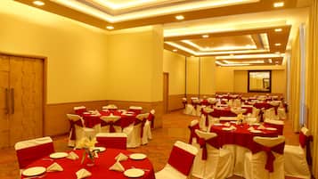 Un salón de banquetes con mesas redondas, sillas blancas adornadas con cintas rojas y suelo alfombrado.