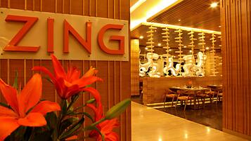 A hotel interior with a wooden reception desk, a sign reading "ZING", and a seating area with tables and chairs.