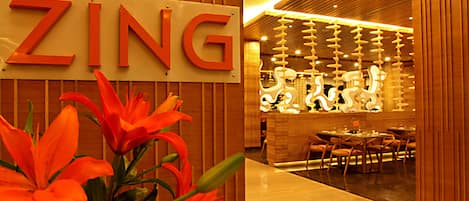 A hotel interior with a wooden reception desk, a sign reading "ZING", and a seating area with tables and chairs.