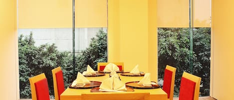 Un comedor con mesa de madera y sillas rojas, ventanas amplias y una lámpara colgante.