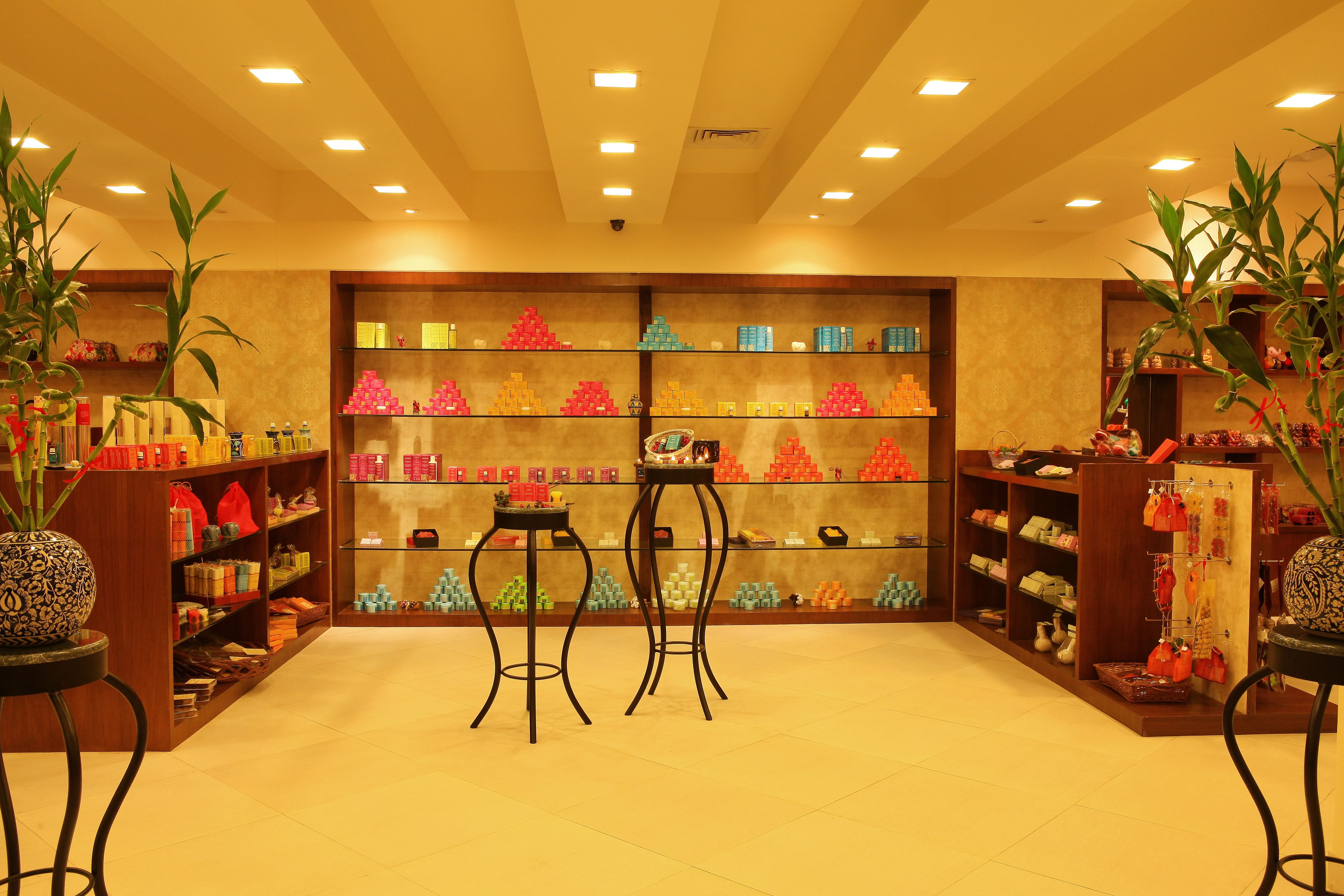 Un espacio comercial bien iluminado con estantes llenos de diversos productos, dos taburetes y plantas decorativas.