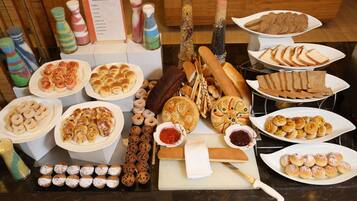 A variety of pastries and baked goods displayed on a table, including donuts, croissants, and bread.