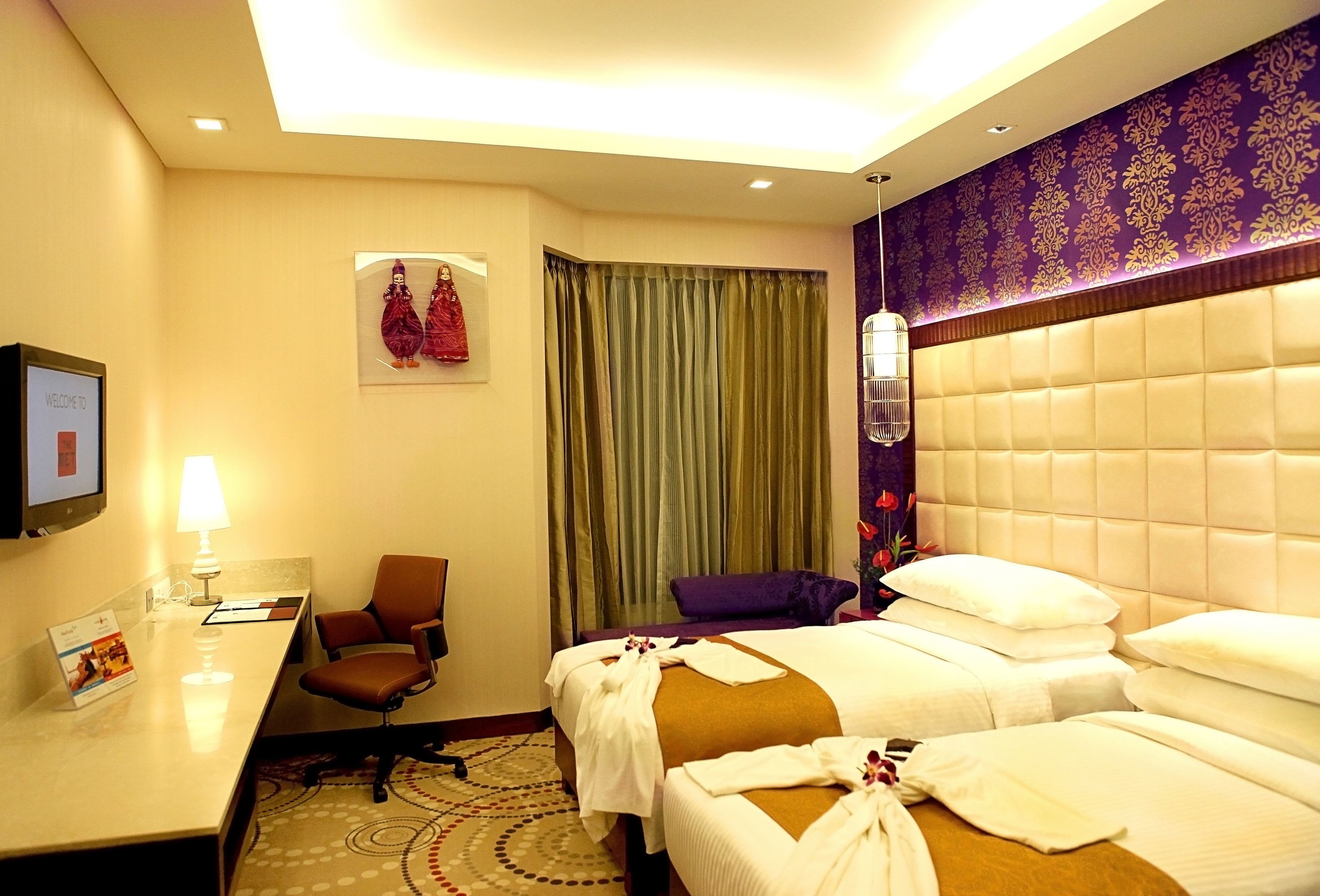 A hotel room with two beds, a desk, a chair, a TV, and a window with curtains.
