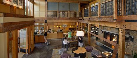 A spacious lobby with a high ceiling, wooden beams, a fireplace, and a reception desk.