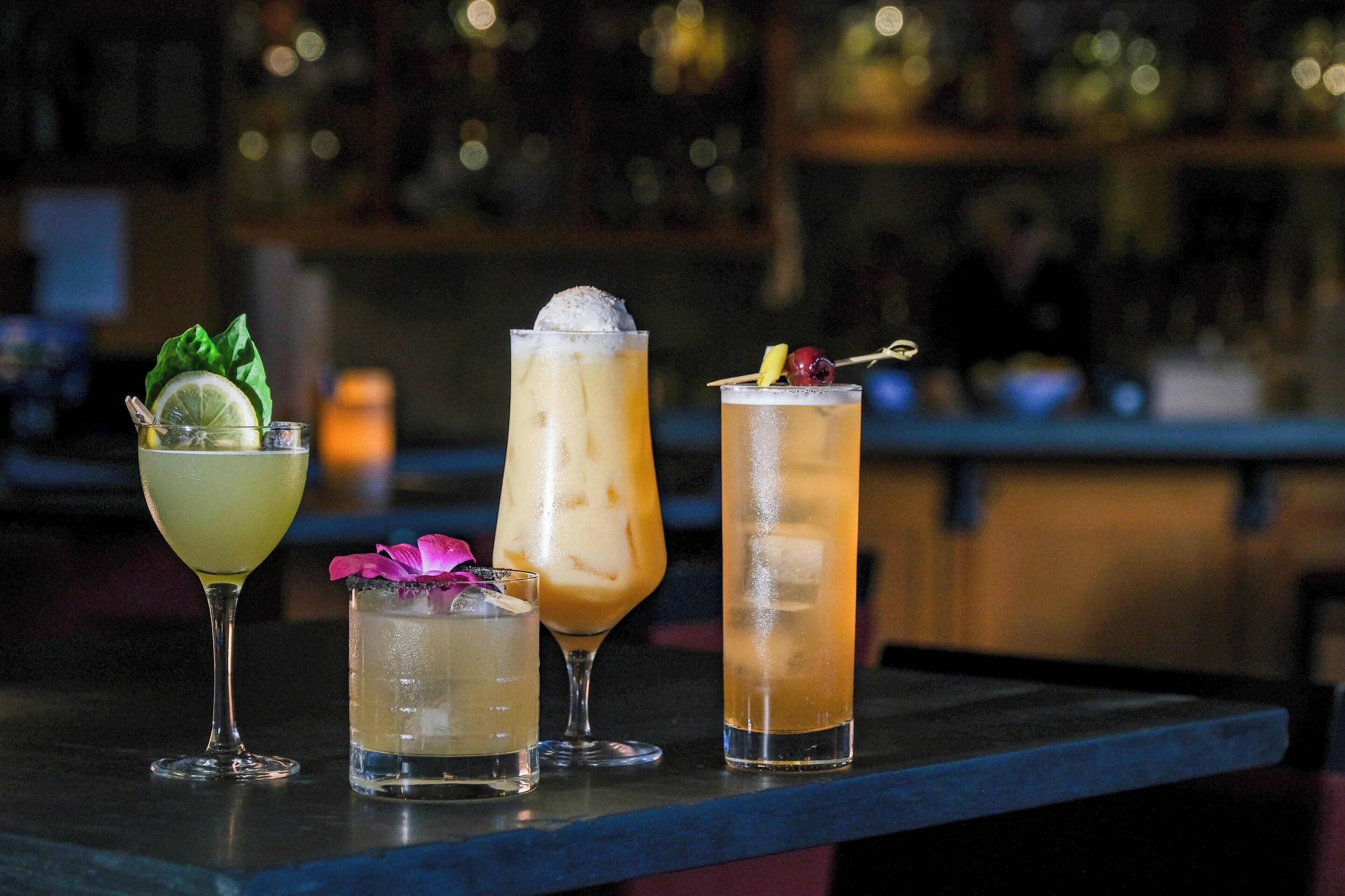 Quatre cocktails différents présentés sur le comptoir d’un bar.