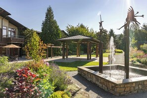 A garden with a fountain, a gazebo, and a building with a balcony.