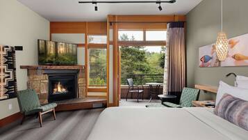 A hotel room with a fireplace, a television, a bed, a balcony with a table and chairs, and a view of the outdoors.