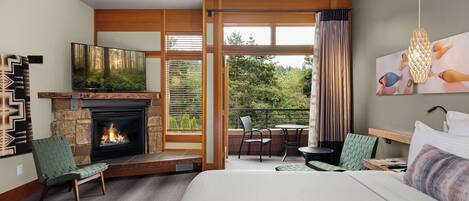 A hotel room with a fireplace, a television, a bed, a balcony with a table and chairs, and a view of the outdoors.
