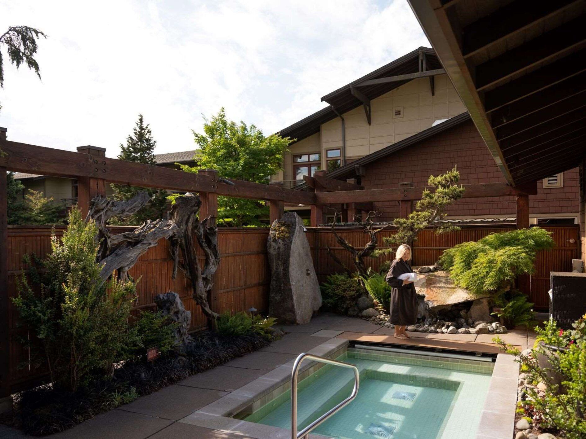 A residential backyard with a swimming pool, wooden pergola, and a stone sculpture.