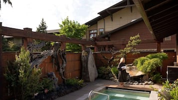A residential backyard with a swimming pool, wooden pergola, and a stone sculpture.
