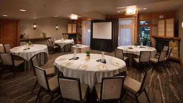 A conference room with multiple round tables, chairs, a projector screen, and a fireplace.