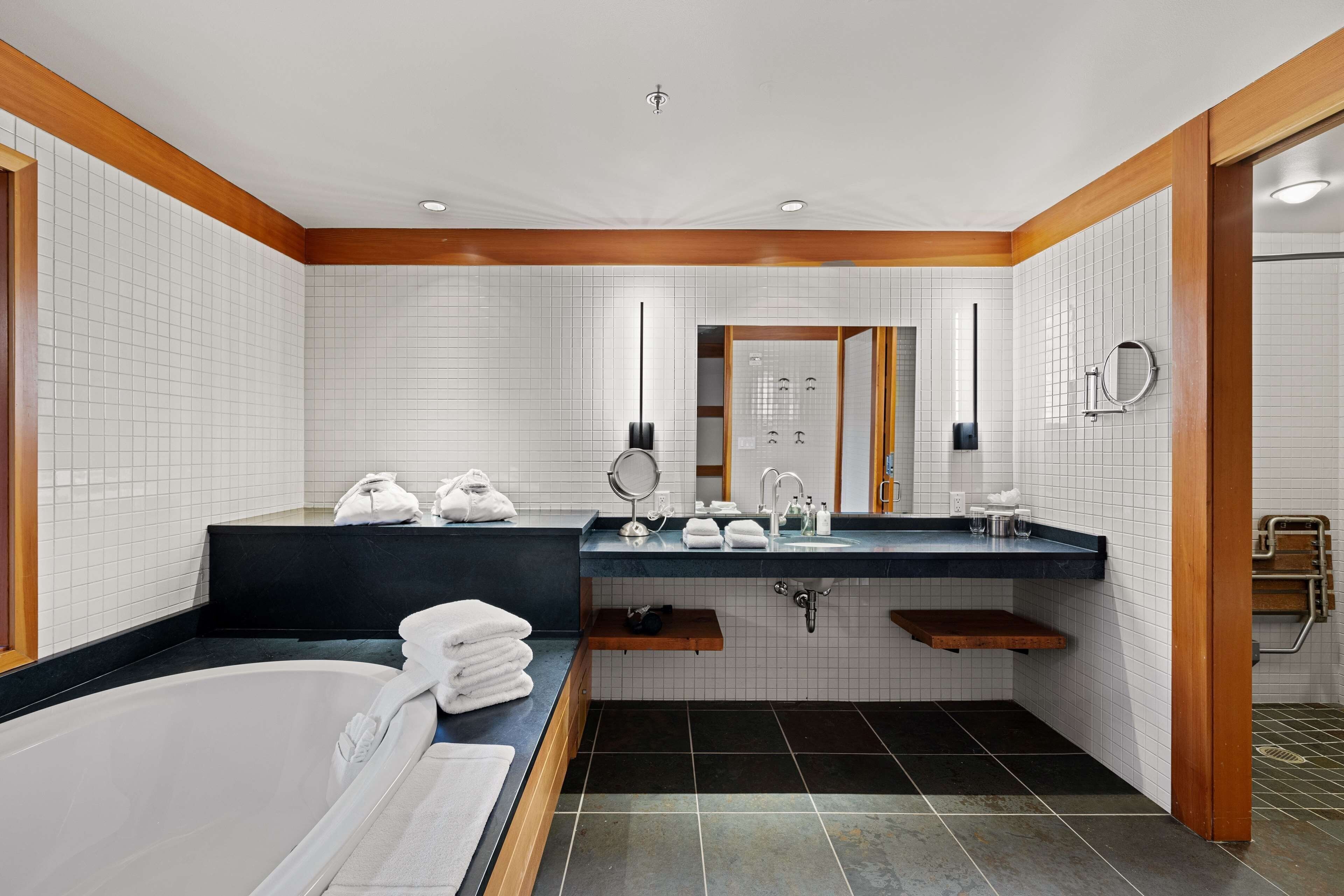 A modern bathroom with a bathtub, two sinks, and a vanity mirror.