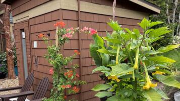 Un bâtiment en bois doté d’un toit en pente, entouré de différentes plantes et fleurs en pot.