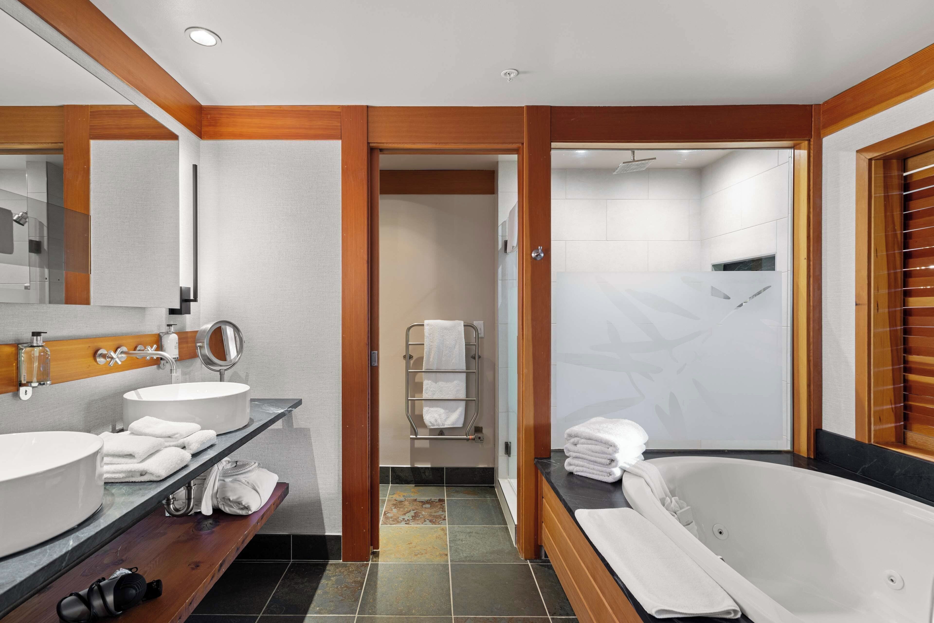 A modern bathroom with two sinks, a large mirror, a bathtub, and a shower area.