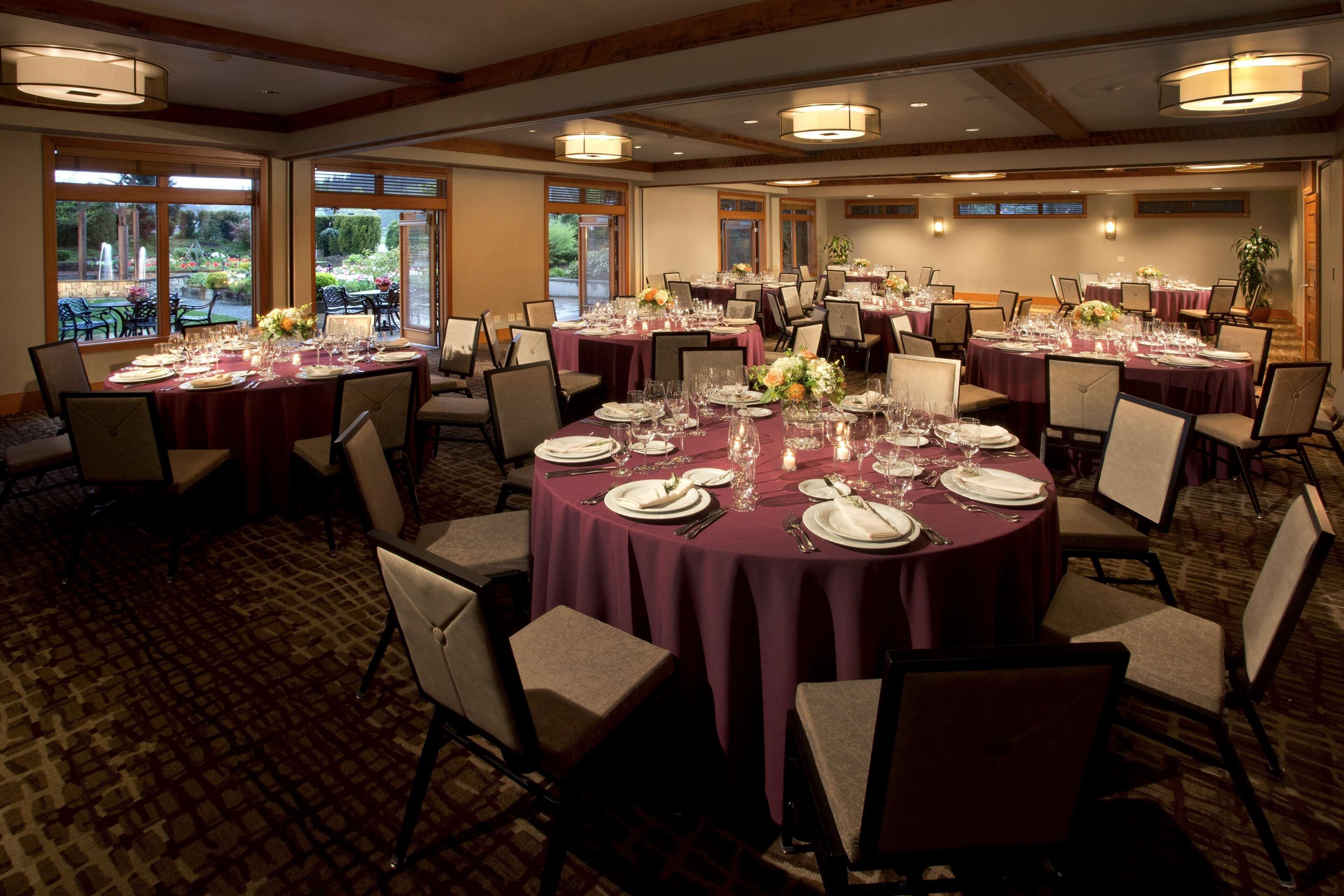 A banquet hall with round tables set for dining, large windows, and a carpeted floor.