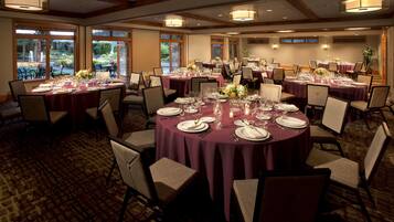 A banquet hall with round tables set for dining, large windows, and a carpeted floor.