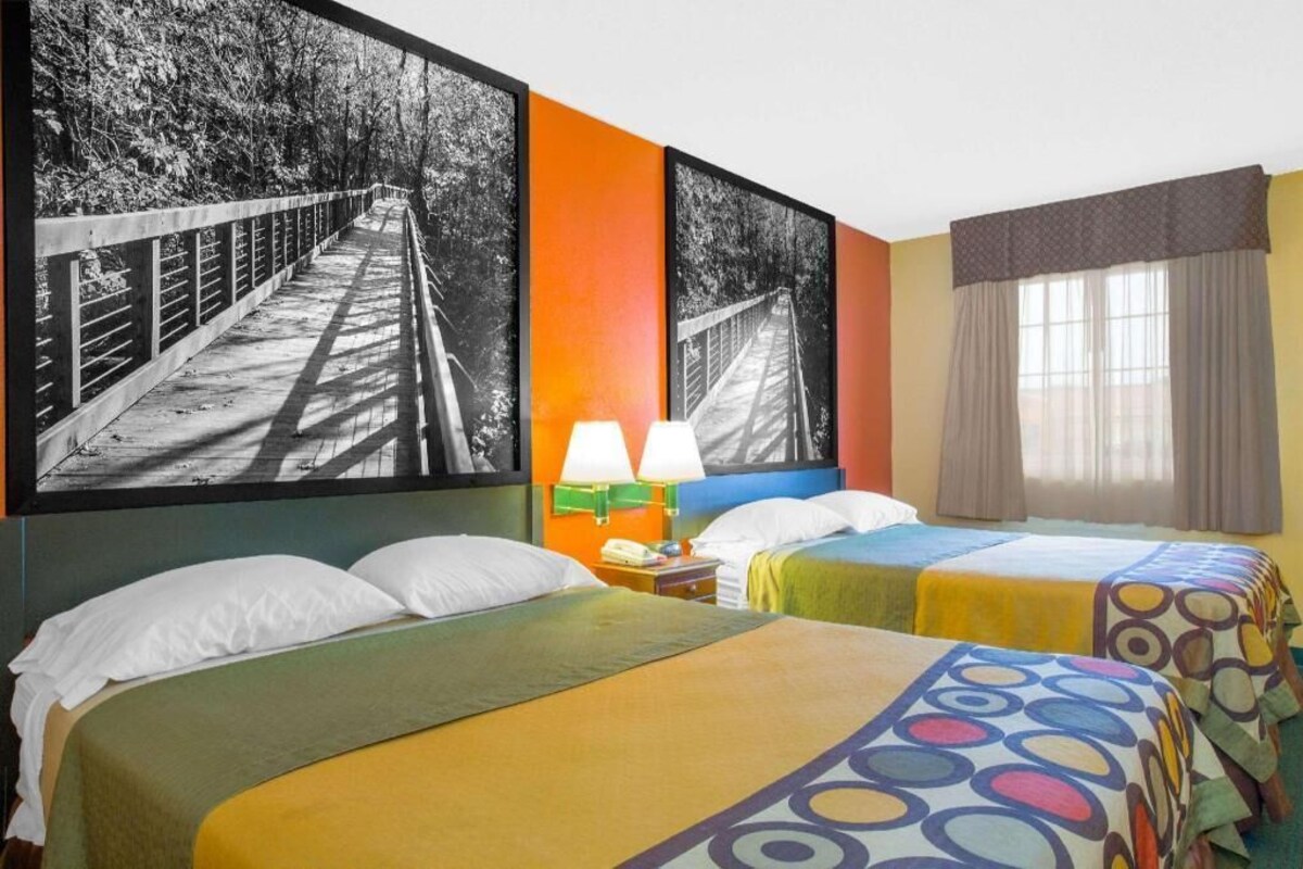A hotel room with two beds, a nightstand, two lamps, and a window with curtains.