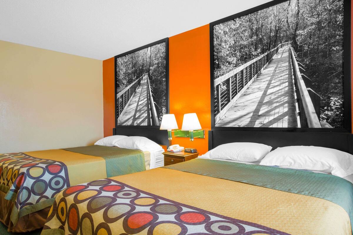 Habitación de hotel con dos camas, una mesita de noche con lámparas y un cuadro grande con un puente.