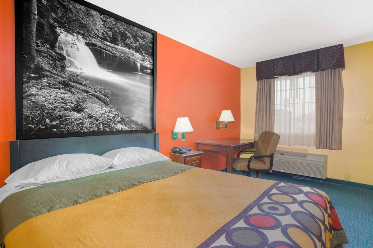 Habitación de hotel con una cama grande, un escritorio, dos lámparas, una silla e impresión enmarcada de una cascada.