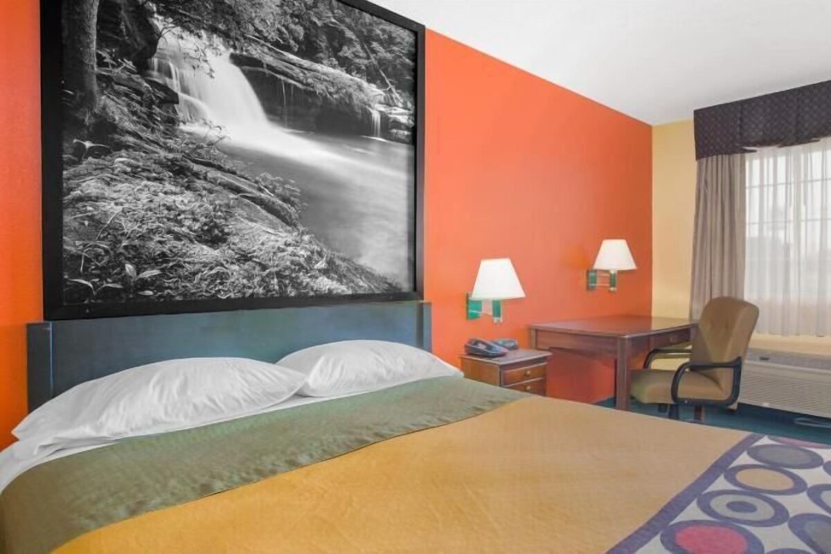 A hotel room with a bed, a desk, a chair, a window with curtains, and a wall-mounted picture of a waterfall.